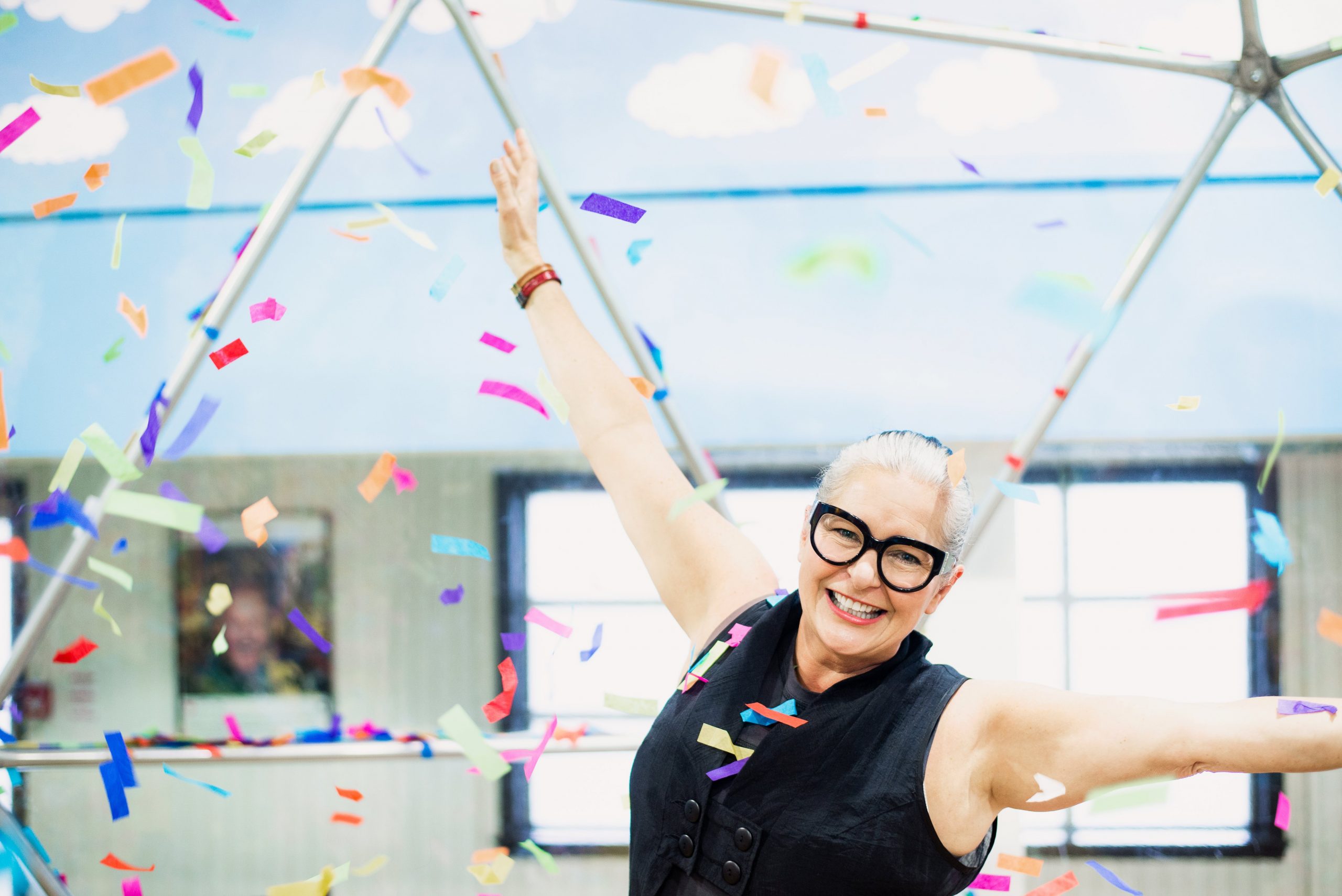 woman throws arms in air as rainbow confetti falls around her scaled