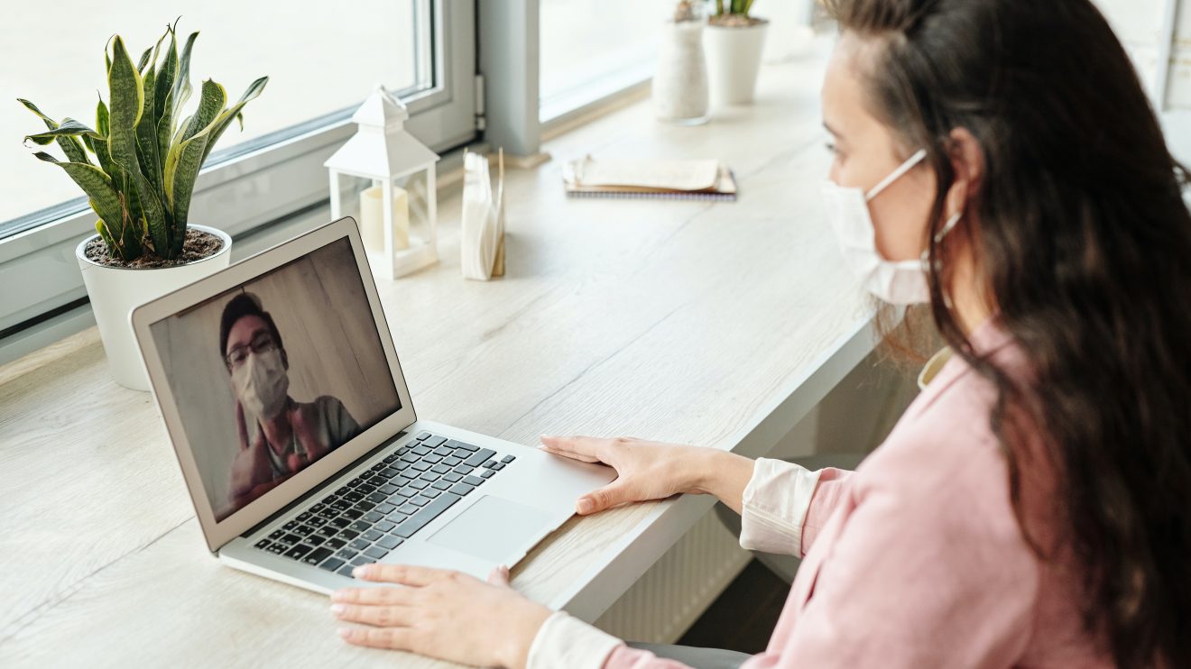 A woman using a laptop for a video call with a man. Both the man and the woman are wearing face masks.