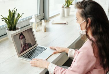 A woman using a laptop for a video call with a man. Both the man and the woman are wearing face masks.