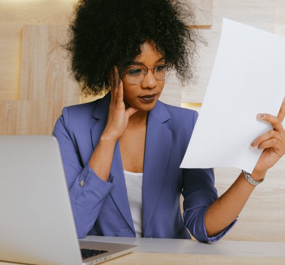 A photograph of a businesswoman staring at a piece of paper and looking confused