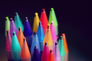 The image shows many different colored pens in front of a black background.