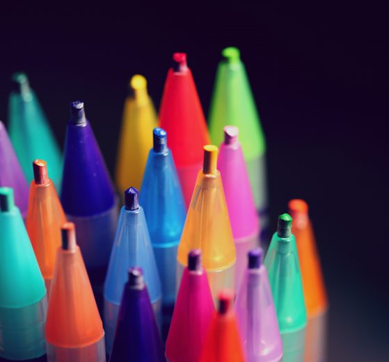 The image shows many different colored pens in front of a black background.