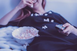 The image shows a woman lying in bed eating popcorn.