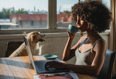 Woman on laptop sipping coffee with her dog