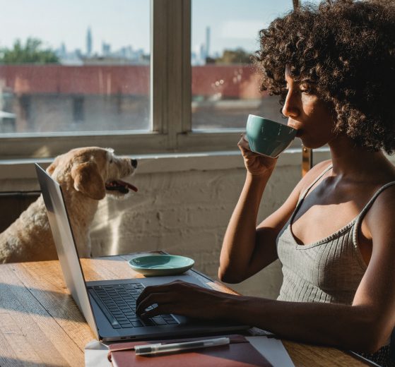 Woman on laptop sipping coffee with her dog