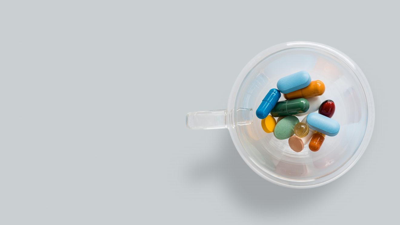 Bird's-eye-view of a plastic cup of colorful pills, representing psychedelic medicine