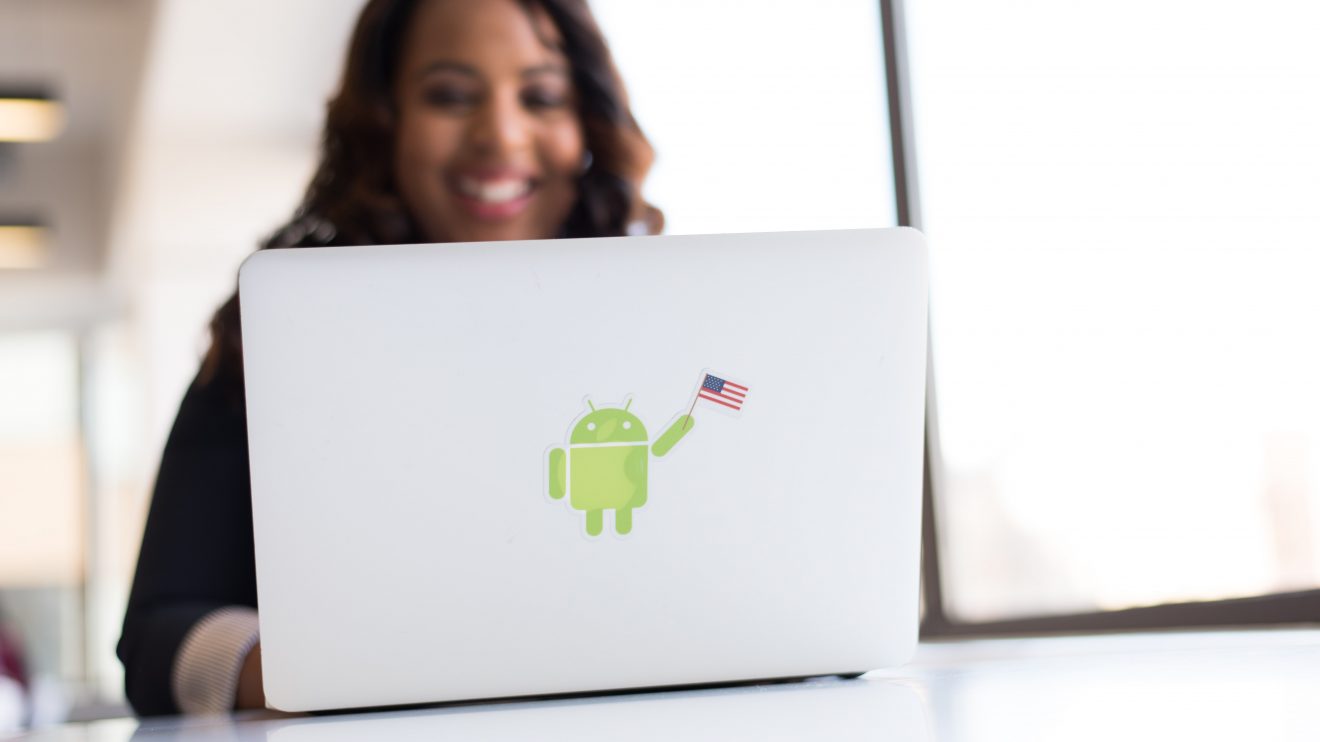 Smiling woman using laptop with android sticker, representing women in tech