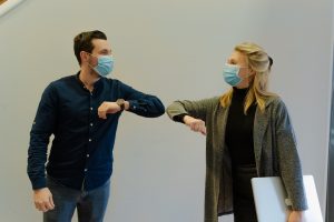 A woman and man at work, wearing masks and bumping elbows