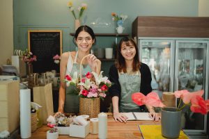 Two women standing and smiling behind a counter at a flower shop, representing women-led businesses
