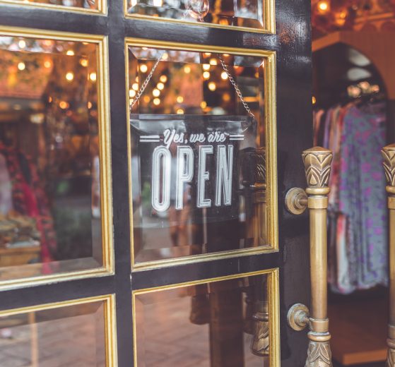An ajar shop door with a "Yes, we are open" sign on it