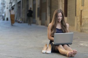 Woman sitting on ground using laptop with her heels beside her