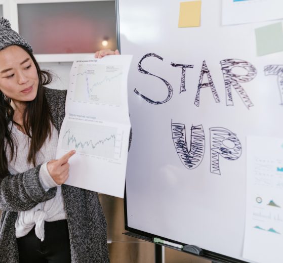 Woman standing in front of whiteboard that says "startup," holding data