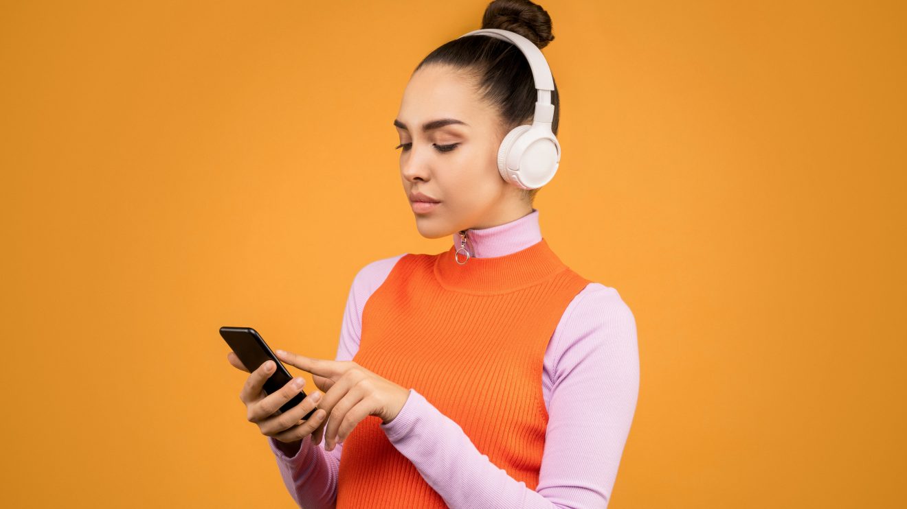 A woman wearing headphones and holding a cellphone