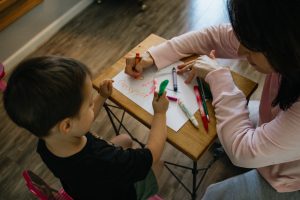 Woman and boy coloring at a table, representing child care centers