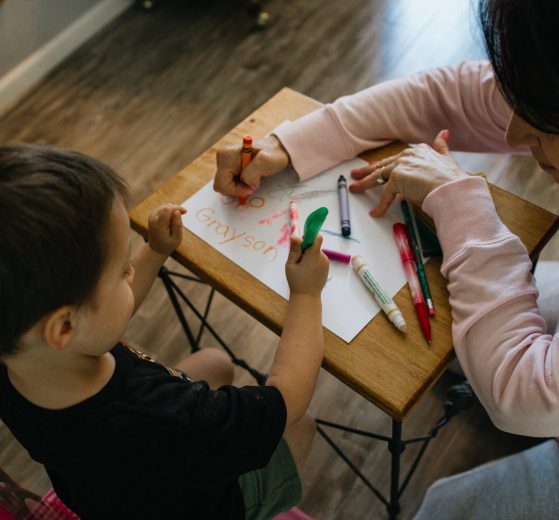 Woman and boy coloring at a table, representing child care centers