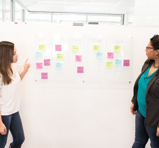 Two women talking beside a white board