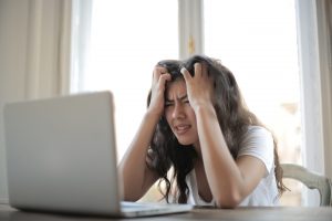 Woman sitting at laptop with her hands in her hair in frustration, representing workplace wellbeing