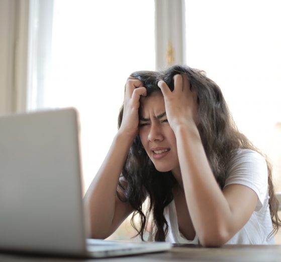 Woman sitting at laptop with her hands in her hair in frustration, representing workplace wellbeing