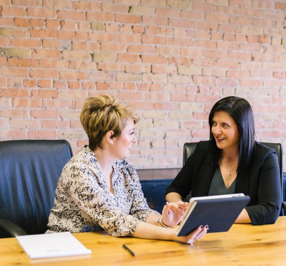 Woman showing another woman something on a tablet, representing mentorship