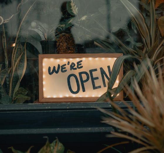 "We're Open" sign in a small business's window surrounded by plants
