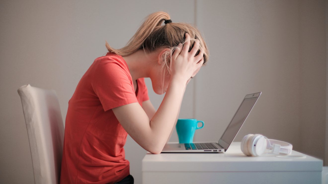 Side view of woman sitting at laptop with head in her hands, representing the Uprise Health survey on employee mental health