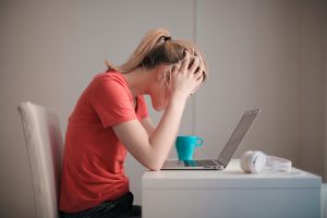 Side view of woman sitting at laptop with head in her hands, representing the Uprise Health survey on employee mental health
