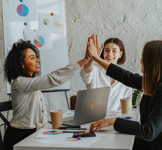 Three women high-five at a table together, representing winning women