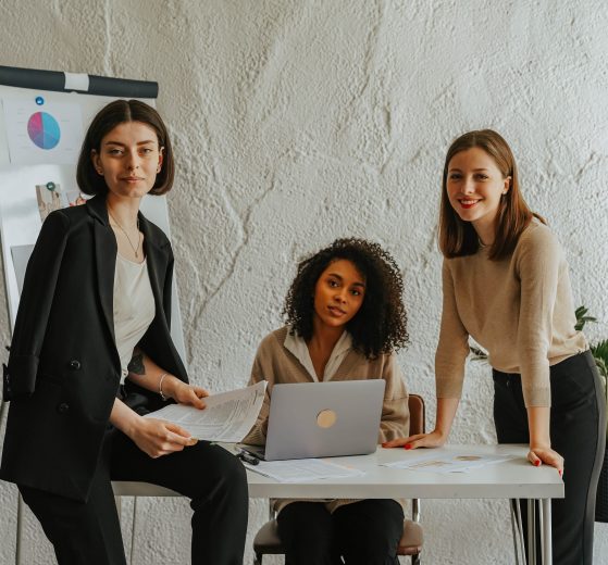 Three women around a white table in an office, representing women business owners
