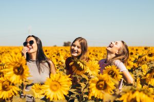 Three young women, laughing in a field of sunflowers, representing Girls With Impact
