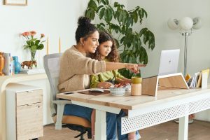 Woman in office, pointing to her laptop, with daughter on her lap, representing working moms