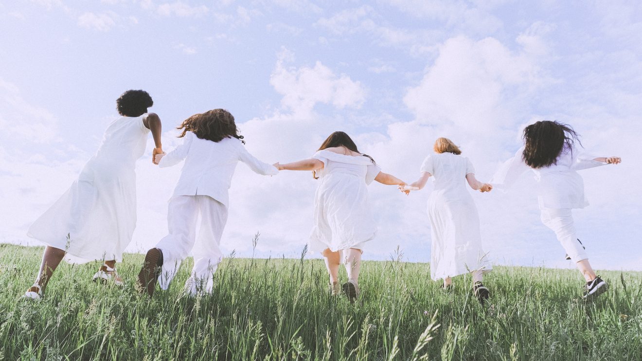 Five women holding hands while running in a field