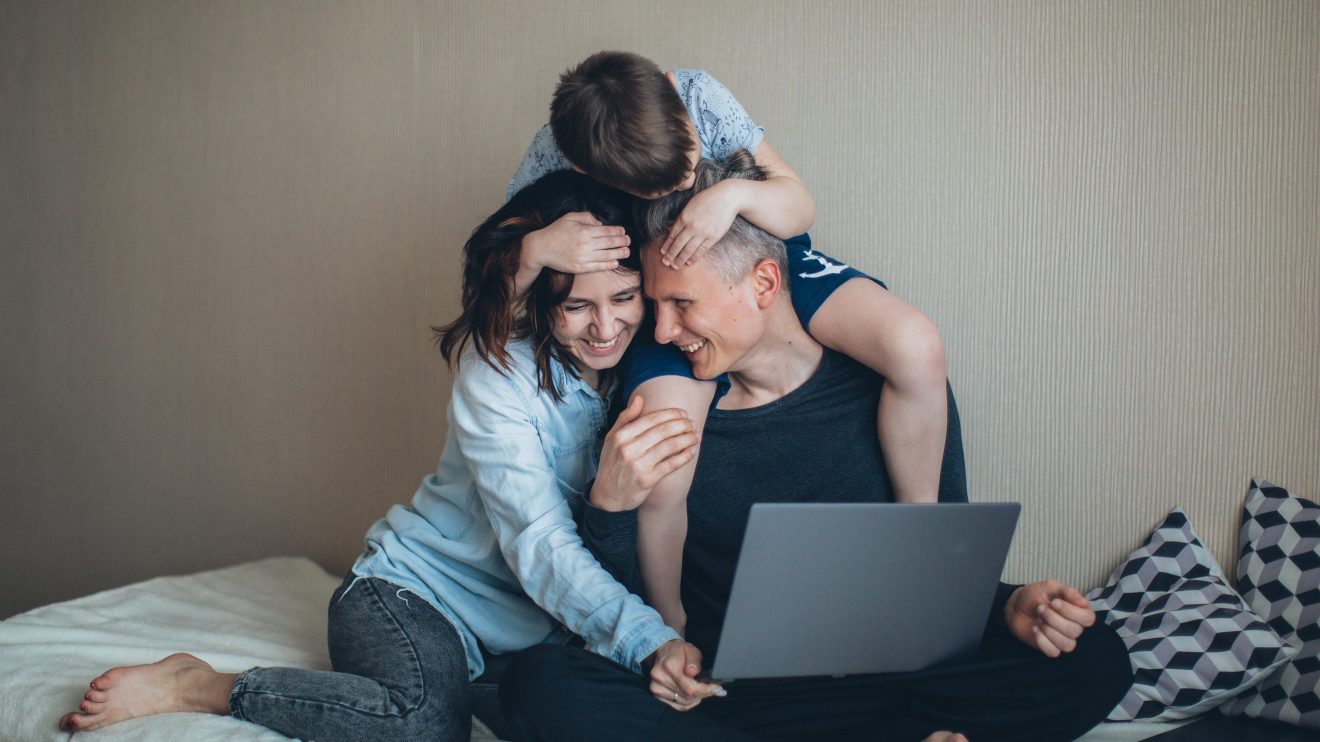 Two moms on a laptop embracing their son, representing working parents