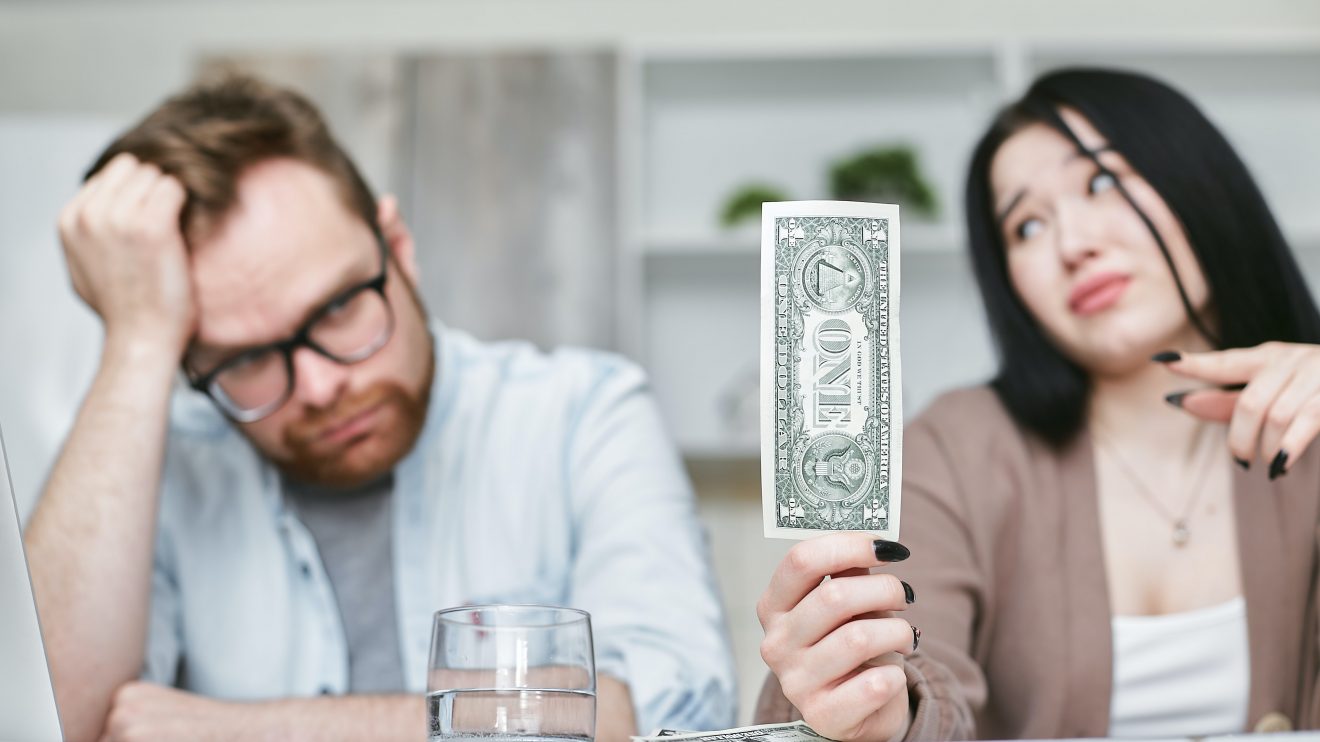 Woman holding up a dollar for man, representing financial wellness