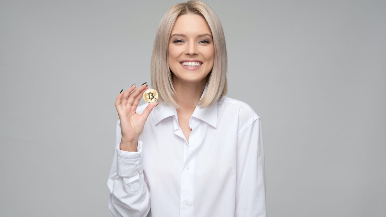 Smiling woman holding up a Bitcoin, representing women in crypto