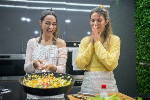 Two women laughing while cooking with a frying pan, representing female food entrepreneurs
